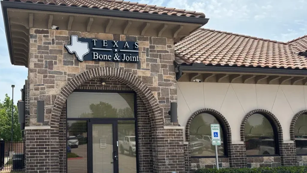 A Texas Bone and Joint clinic building, stone and brick with a tiled roof and an arched entrance under the practice sign